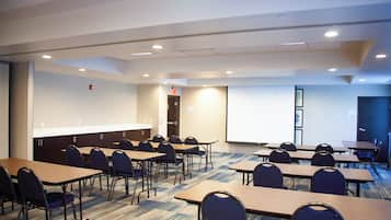 A conference room with multiple tables and chairs, a projector screen, and a carpeted floor.