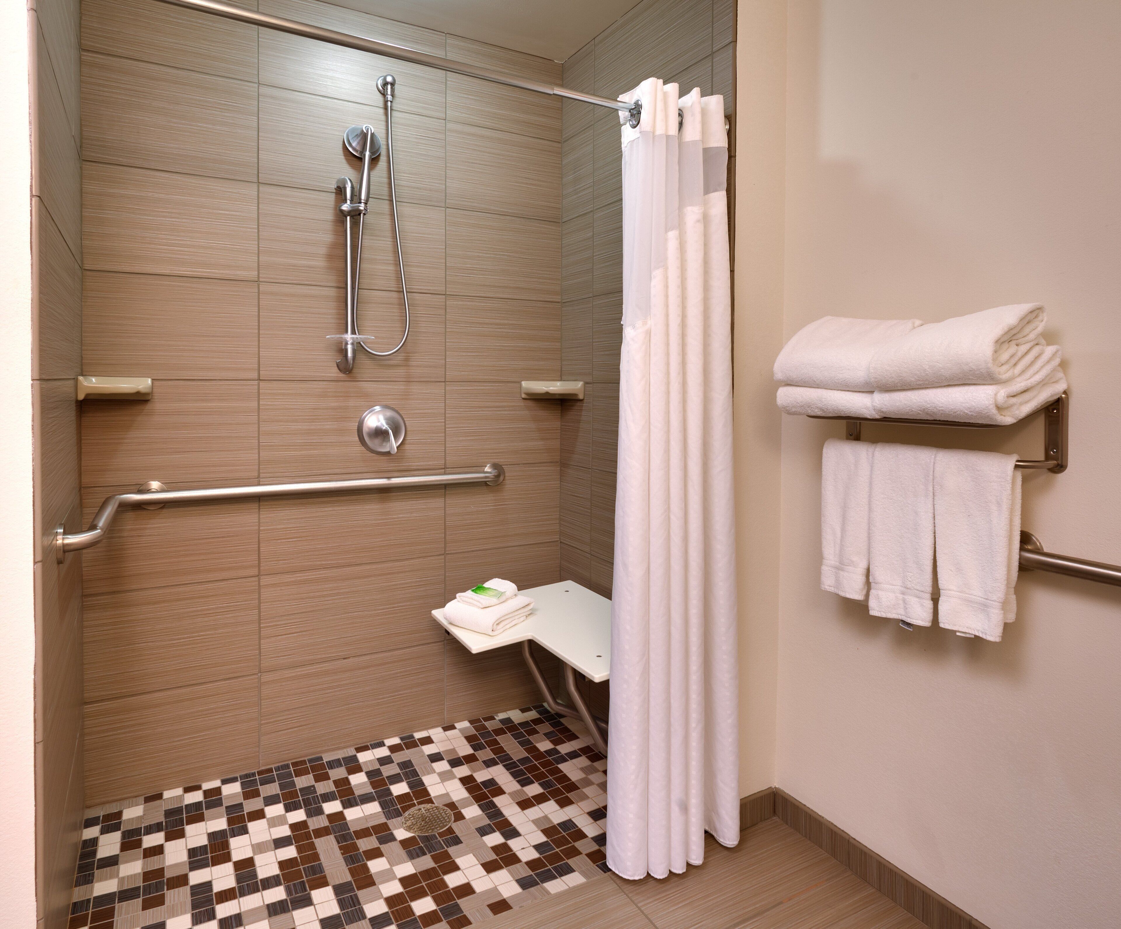 A shower area with a handrail, a showerhead, and a tiled floor.