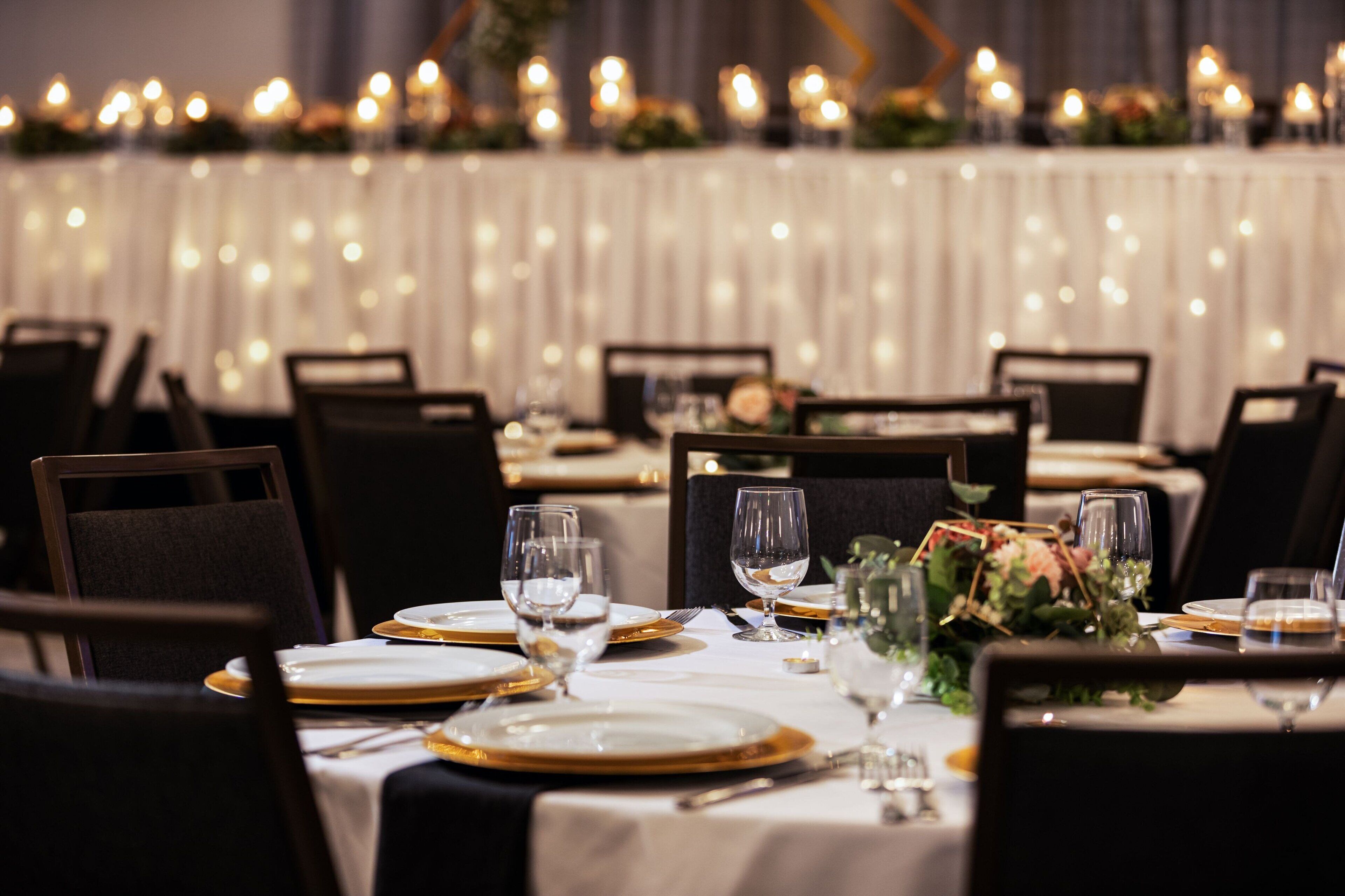 A dining area with tables set for a meal, featuring white tablecloths, gold-rimmed plates, and clear glassware.