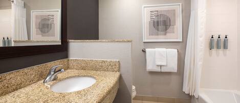 Une salle de bain moderne avec un lavabo en granit, un miroir, une douche et deux œuvres d’art encadrées accrochées au mur.