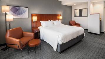Een hotelkamer met een groot bed, twee nachtkastjes met lampen, een bruine leren fauteuil, een klein rond tafeltje en een kunstwerk aan de muur.