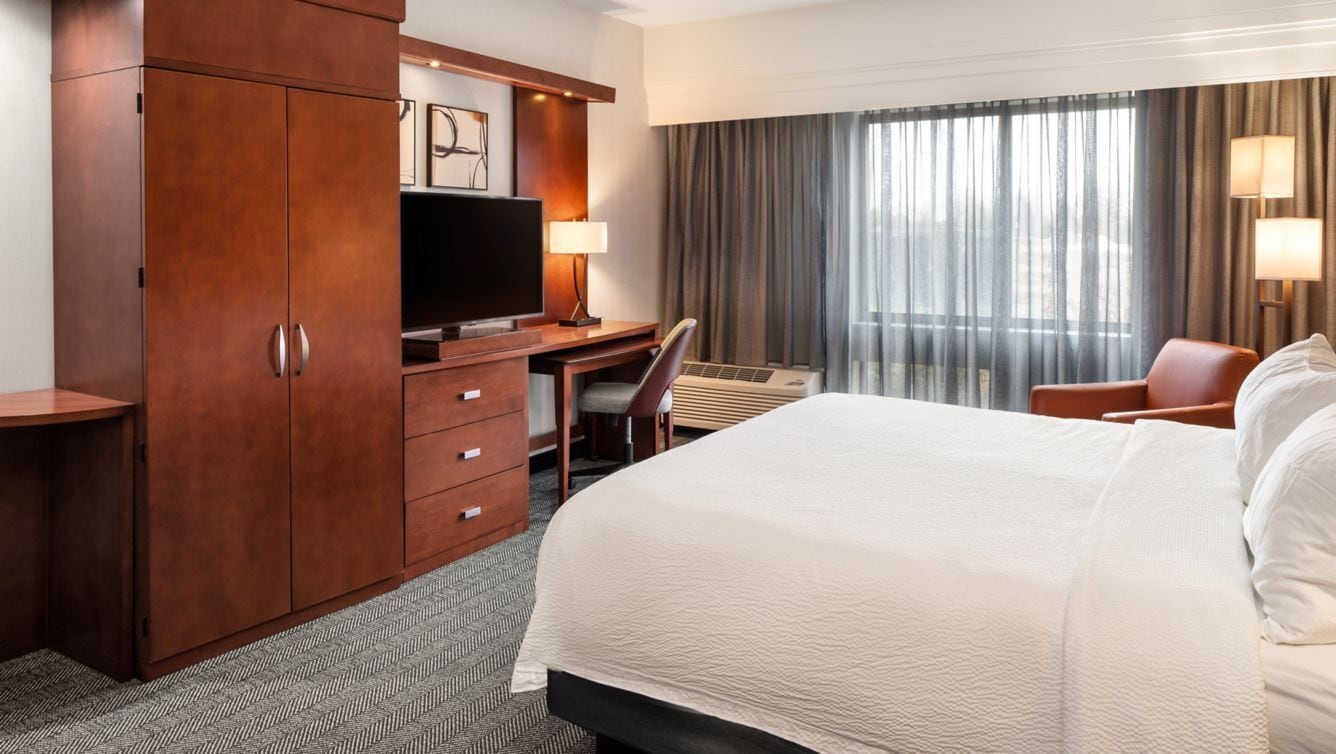 Een hotelkamer met een bed, een bureau, een televisie, een stoel en een kledingkast.