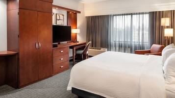 Een hotelkamer met een bed, een bureau, een televisie, een stoel en een kledingkast.
