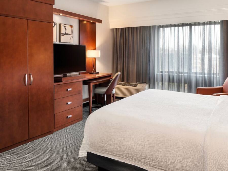 Een hotelkamer met een bed, een bureau, een televisie, een stoel en een kledingkast.