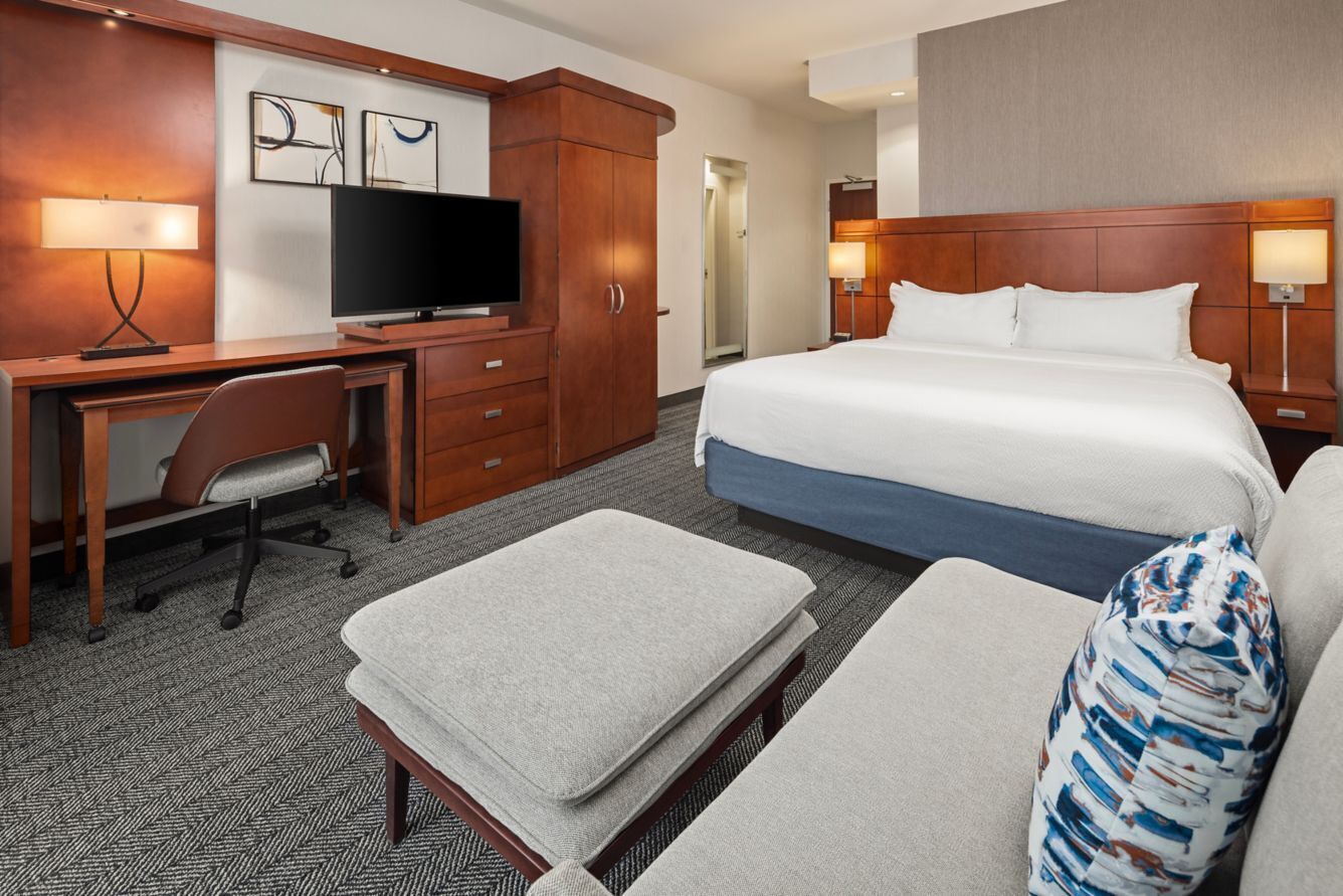 Una habitación de hotel con una cama, un escritorio con televisor, una silla, un sofá y una mesita.