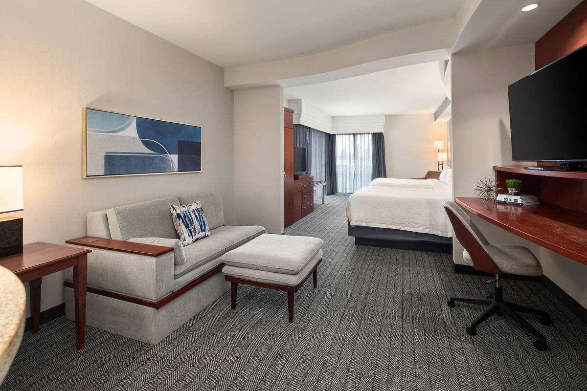 A hotel room with a sofa, a desk, a television, and a bed.