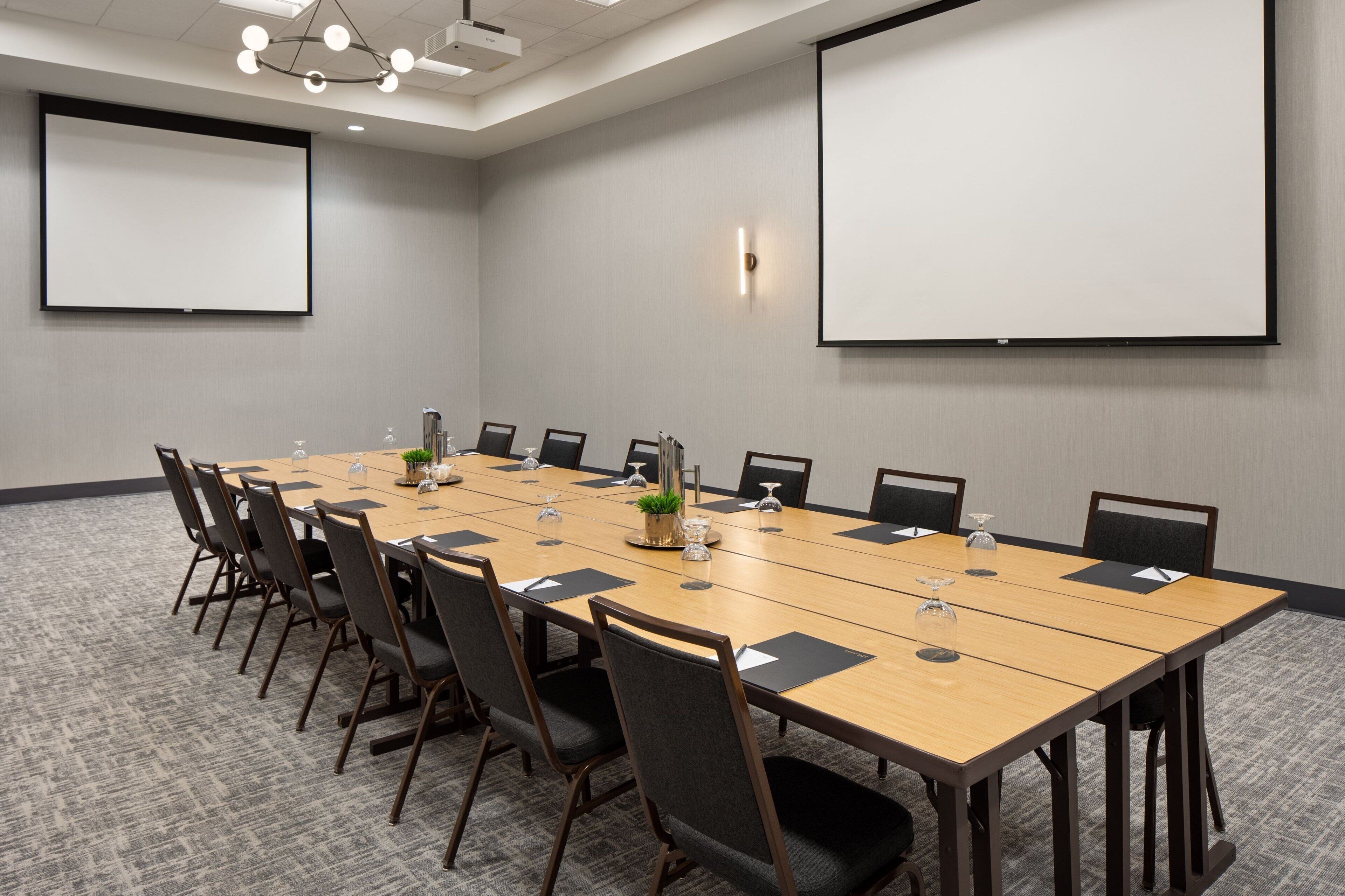 A conference room with a long table, chairs, a projector screen, and a carpeted floor.