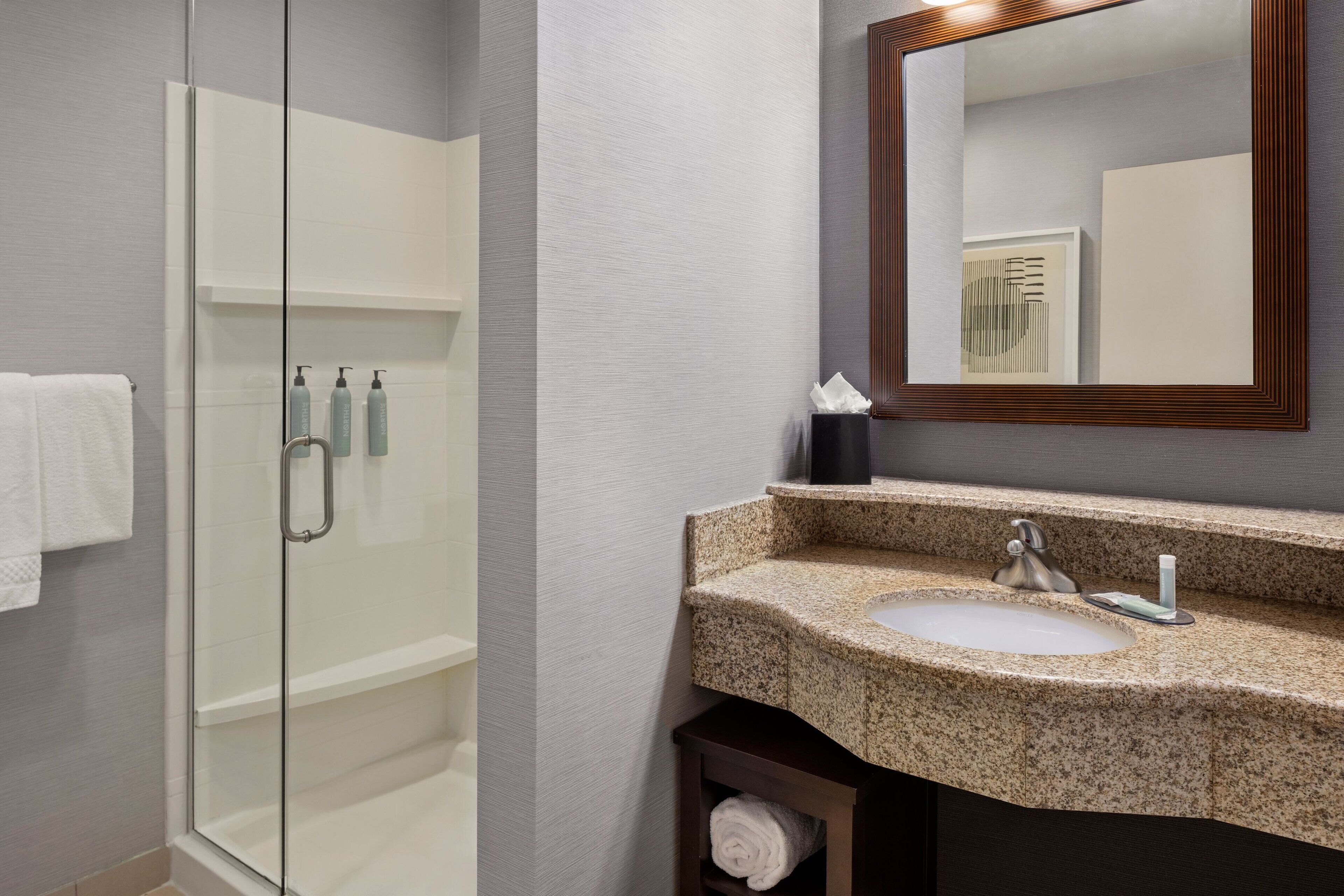 A modern bathroom with a glass-enclosed shower, a granite sink, and a large mirror.