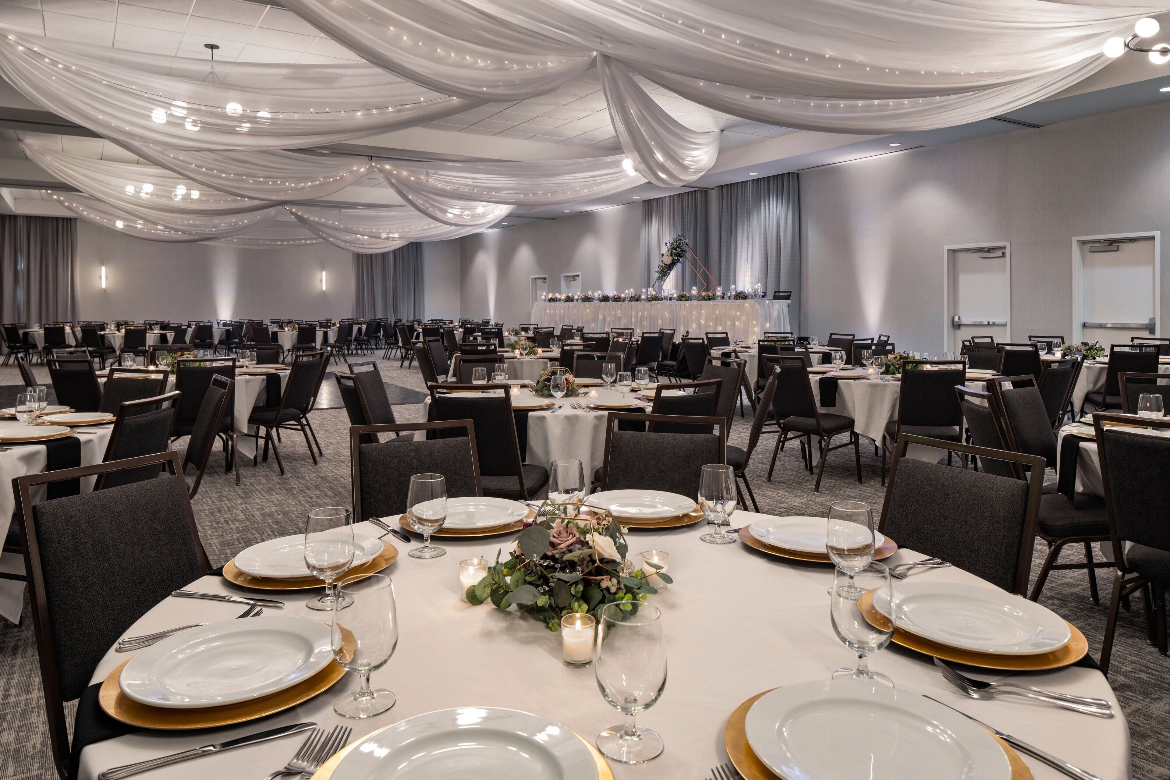 A banquet hall with round tables set for dining, featuring gold-rimmed plates and white tablecloths.