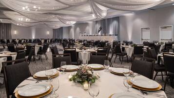 A banquet hall with round tables set for dining, featuring gold-rimmed plates and white tablecloths.