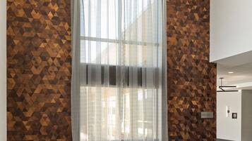 A modern room with geometric patterned walls, a large window with sheer curtains, and two grey armchairs.