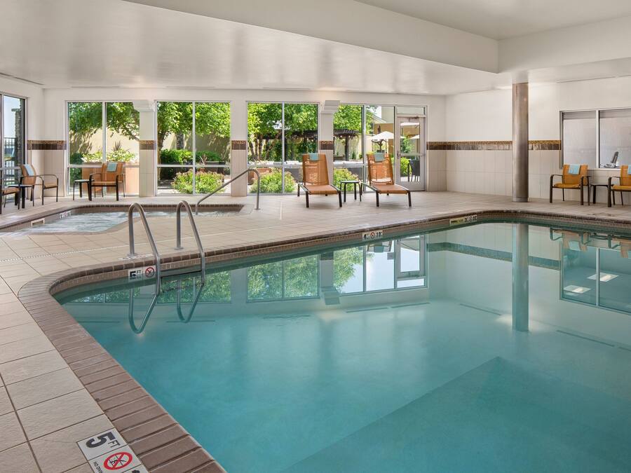 An indoor swimming pool with clear glass walls, sun loungers, and a tiled floor.