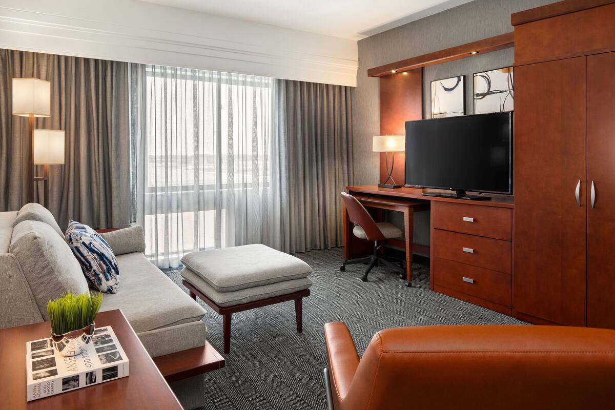 A hotel room with a sofa, ottoman, desk, television, and a cabinet.
