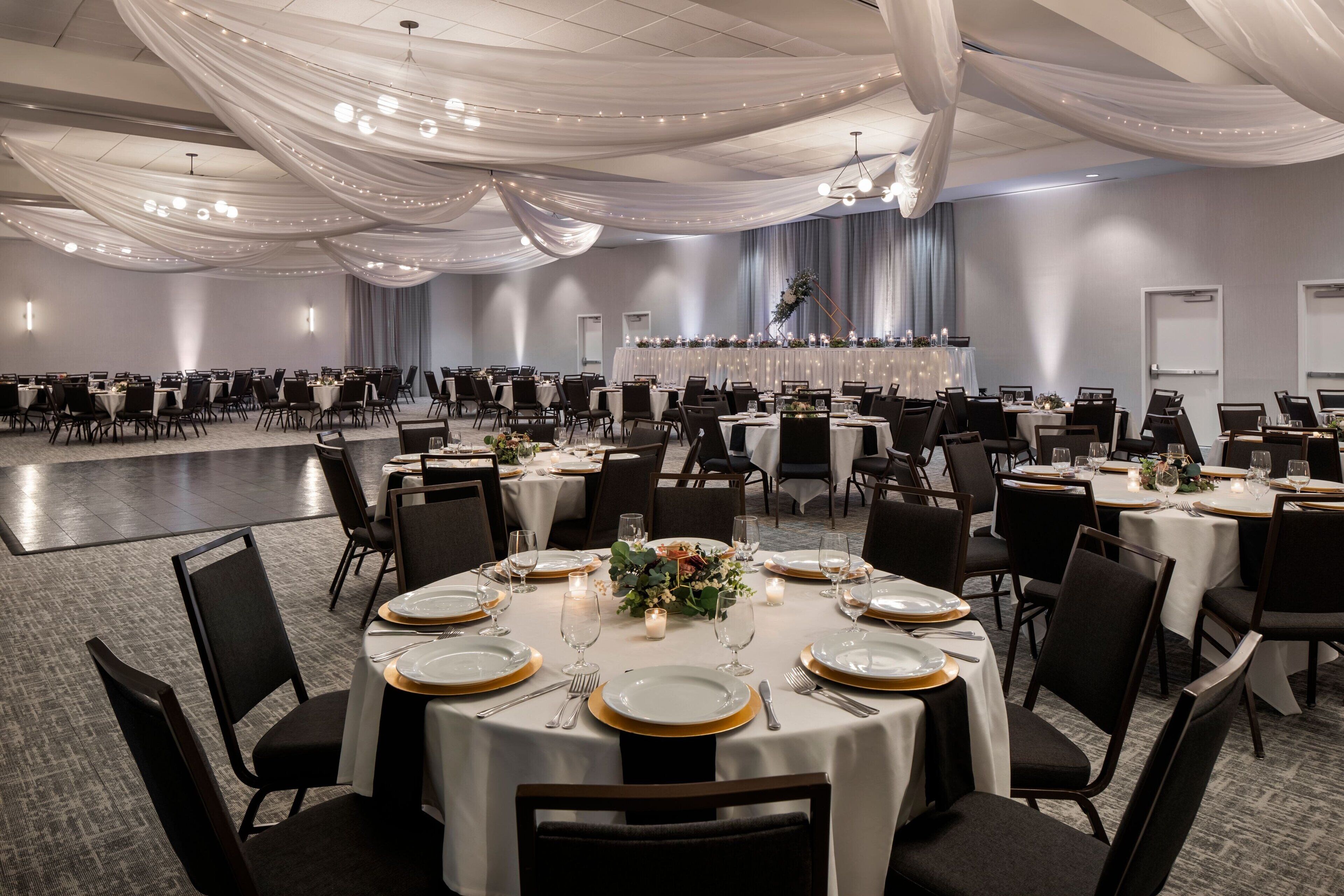 A banquet hall with round tables set for dining, featuring white tablecloths, gold-rimmed plates, and candles.