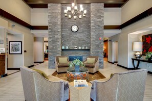 A lobby with a stone wall, a clock, two sofas, a coffee table, and a fireplace. - Homewood Suites by Hilton Doylestown (Warrington)
