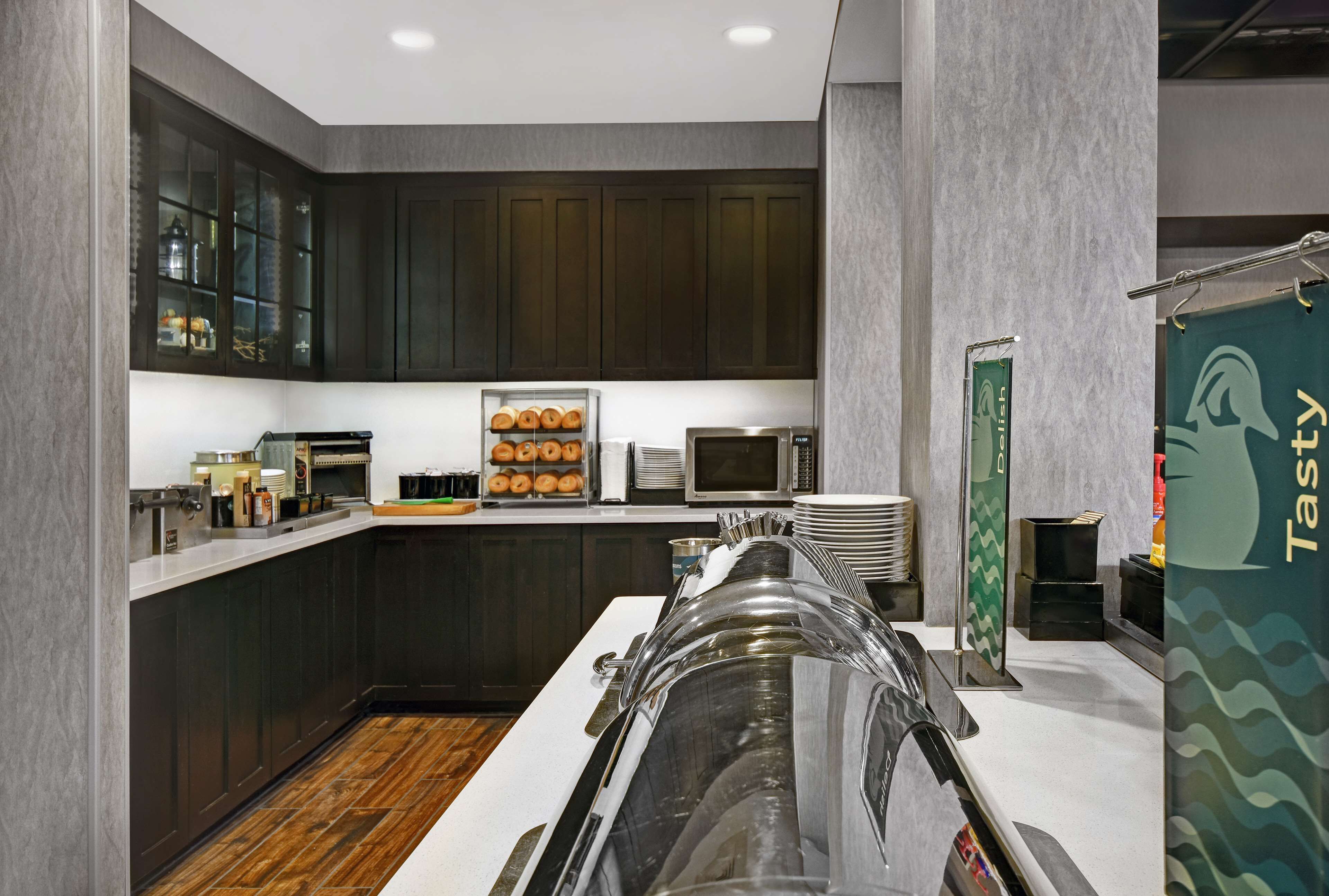 A modern kitchen with dark wooden cabinets, a stainless steel sink, and a glass display case with baked goods.