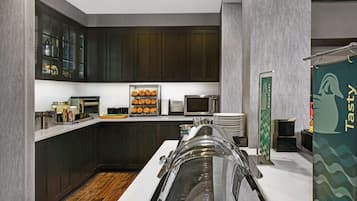 A modern kitchen with dark wooden cabinets, a stainless steel sink, and a glass display case with baked goods.