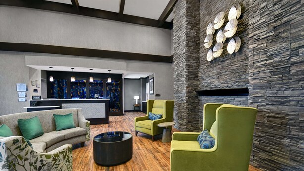 A lobby with a reception desk, green armchairs, a sofa, and a stone accent wall. - Homewood Suites by Hilton Doylestown (Warrington)