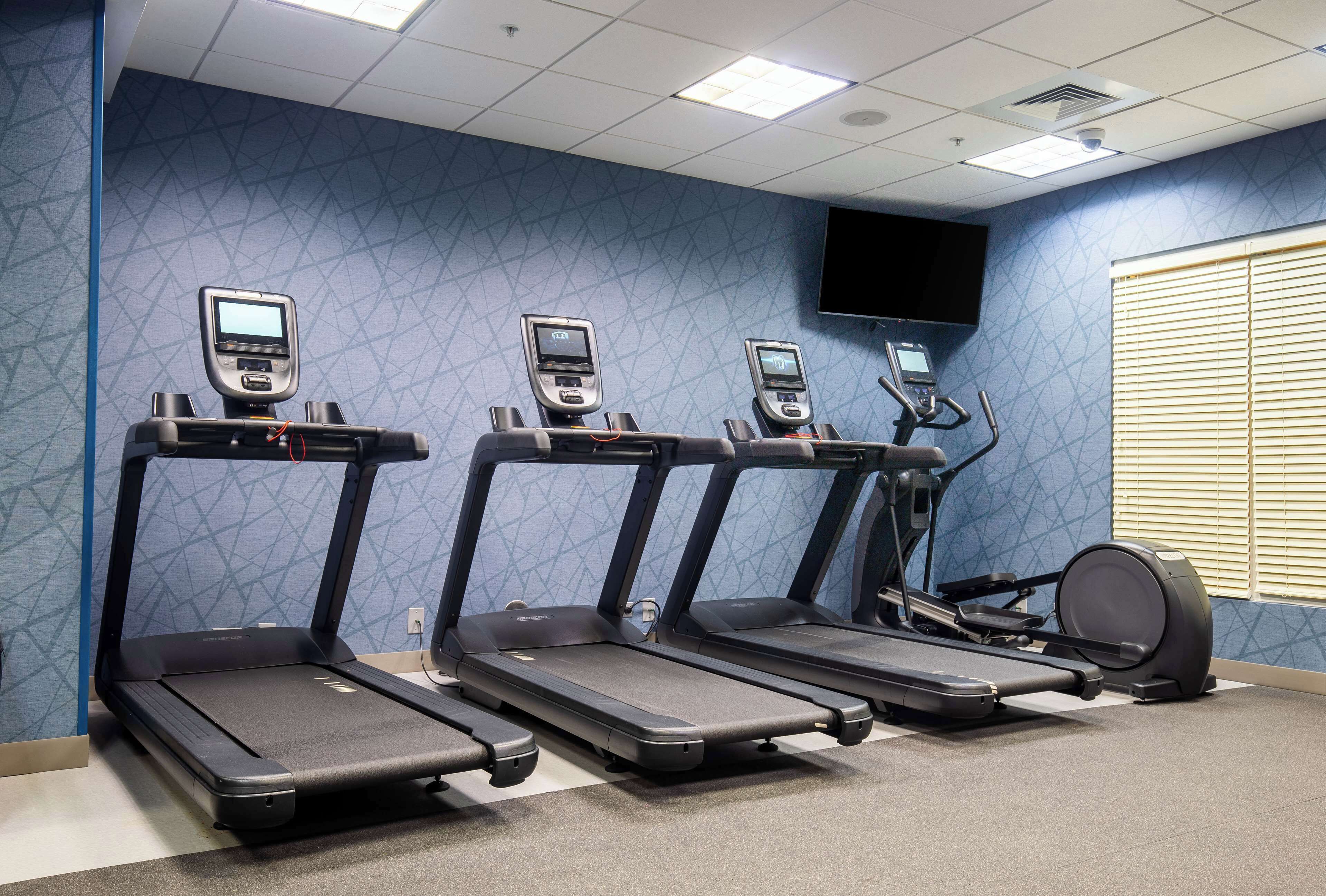 Un gimnasio con cuatro cintas de correr, una máquina elíptica y un televisor montado en la pared.