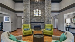 A spacious lobby with a stone fireplace, two green armchairs, a round coffee table, and a chandelier. - Homewood Suites by Hilton Doylestown (Warrington)