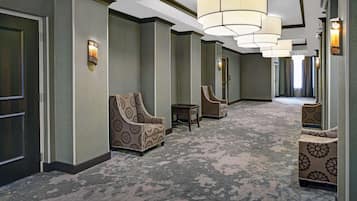 Un corridoio d'hotel con poltrone a fantasia, pavimento rivestito di moquette e un lampadario moderno.