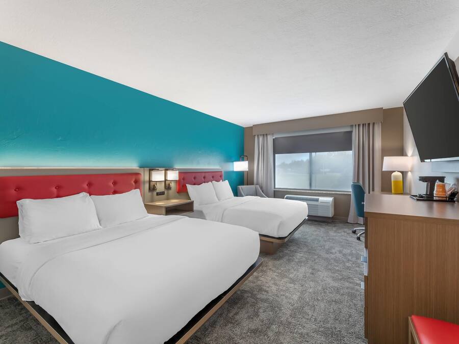 A hotel room with two beds, a desk, a TV, and a window with curtains.