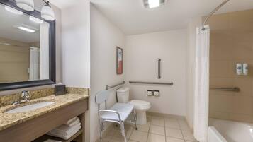 A bathroom with a granite sink, a mirror, a toilet, a shower, and a wheelchair-accessible chair.