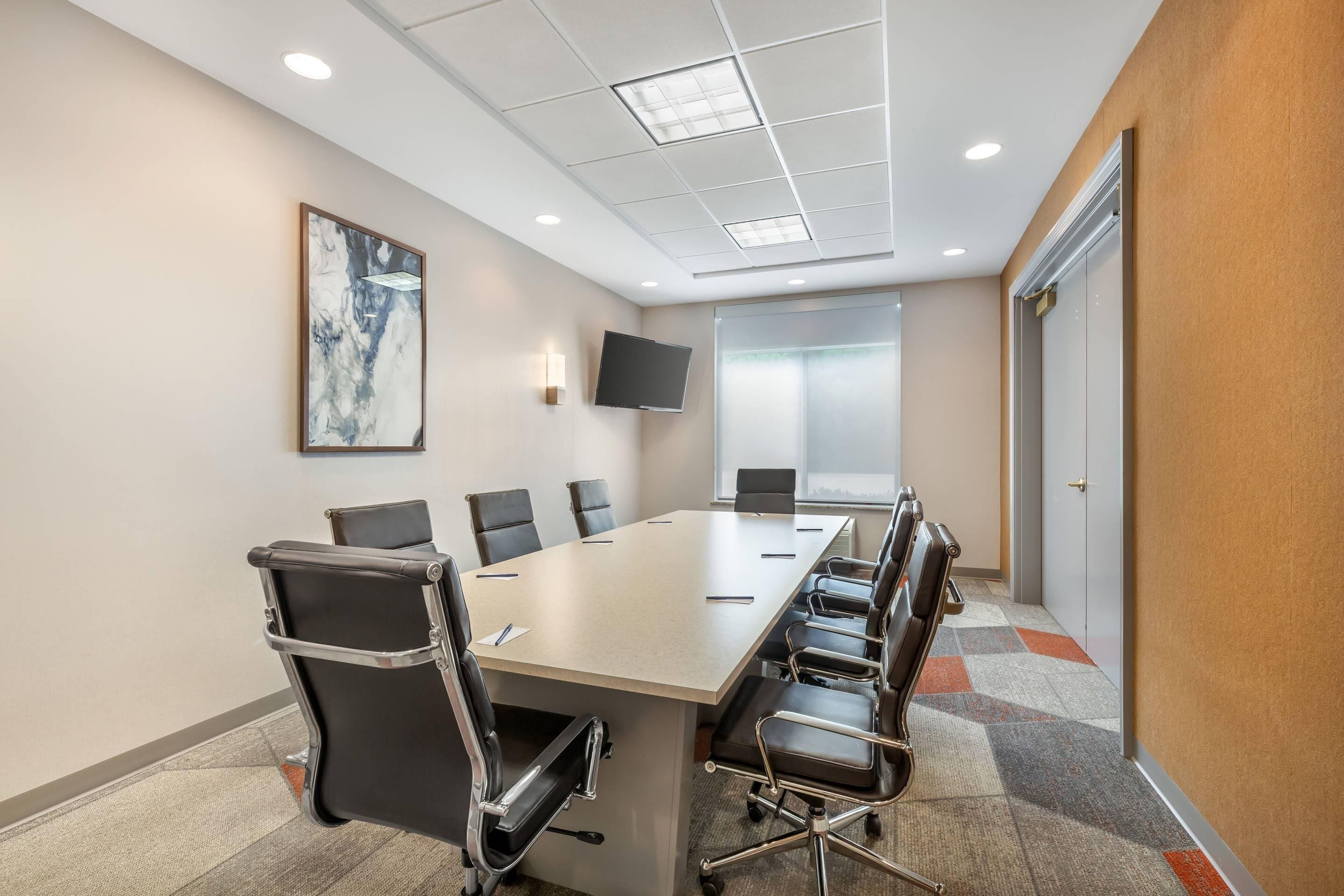 A conference room with a long table, chairs, a flat-screen TV, and a painting on the wall.