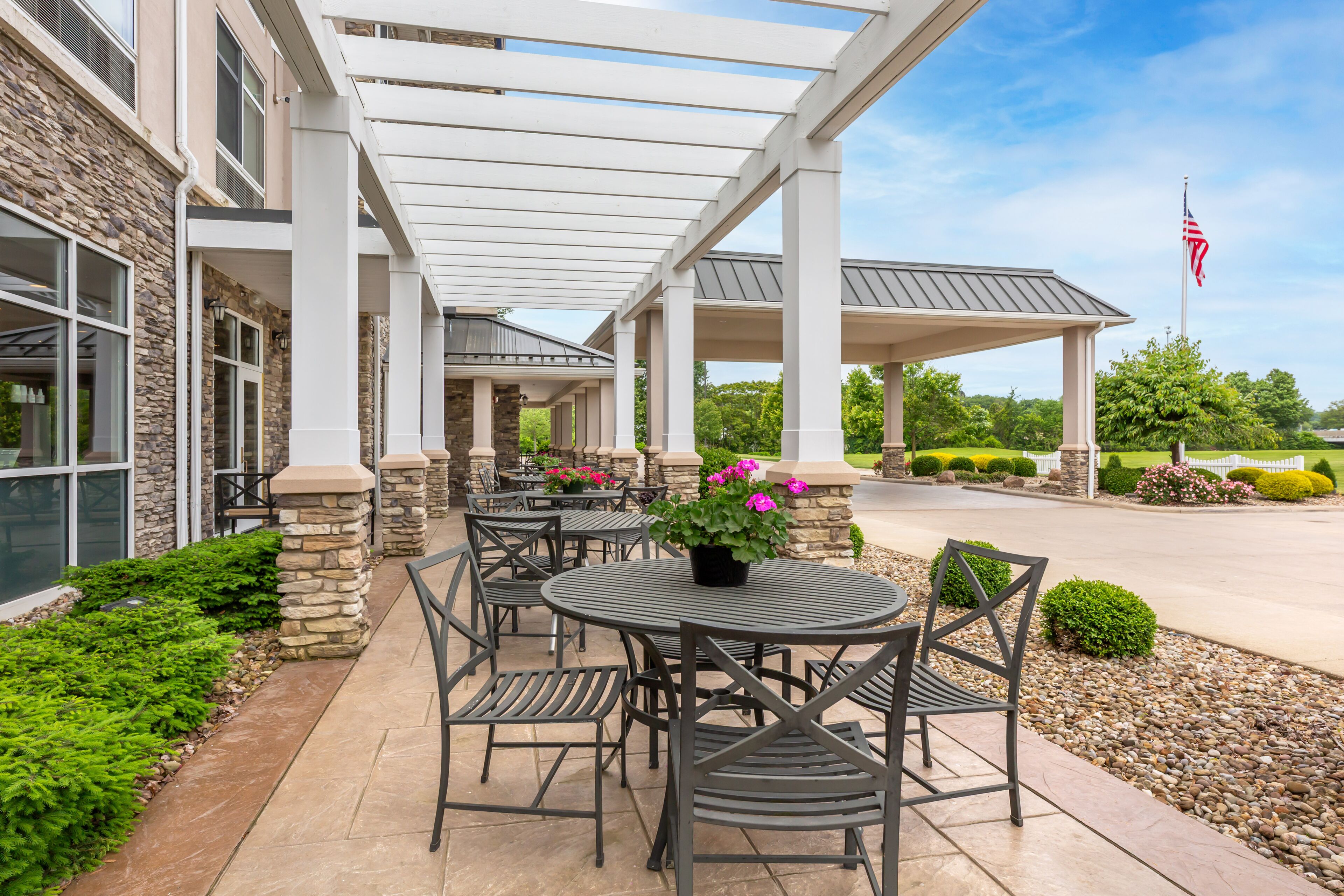 An outdoor patio with tables and chairs, stone pillars, and a covered area with an American flag.