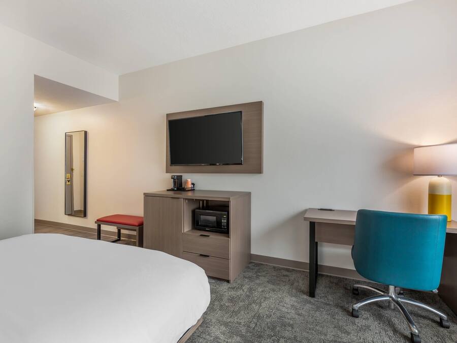 A hotel room with a bed, a desk, a chair, a television, a microwave, a lamp, and a mirror.