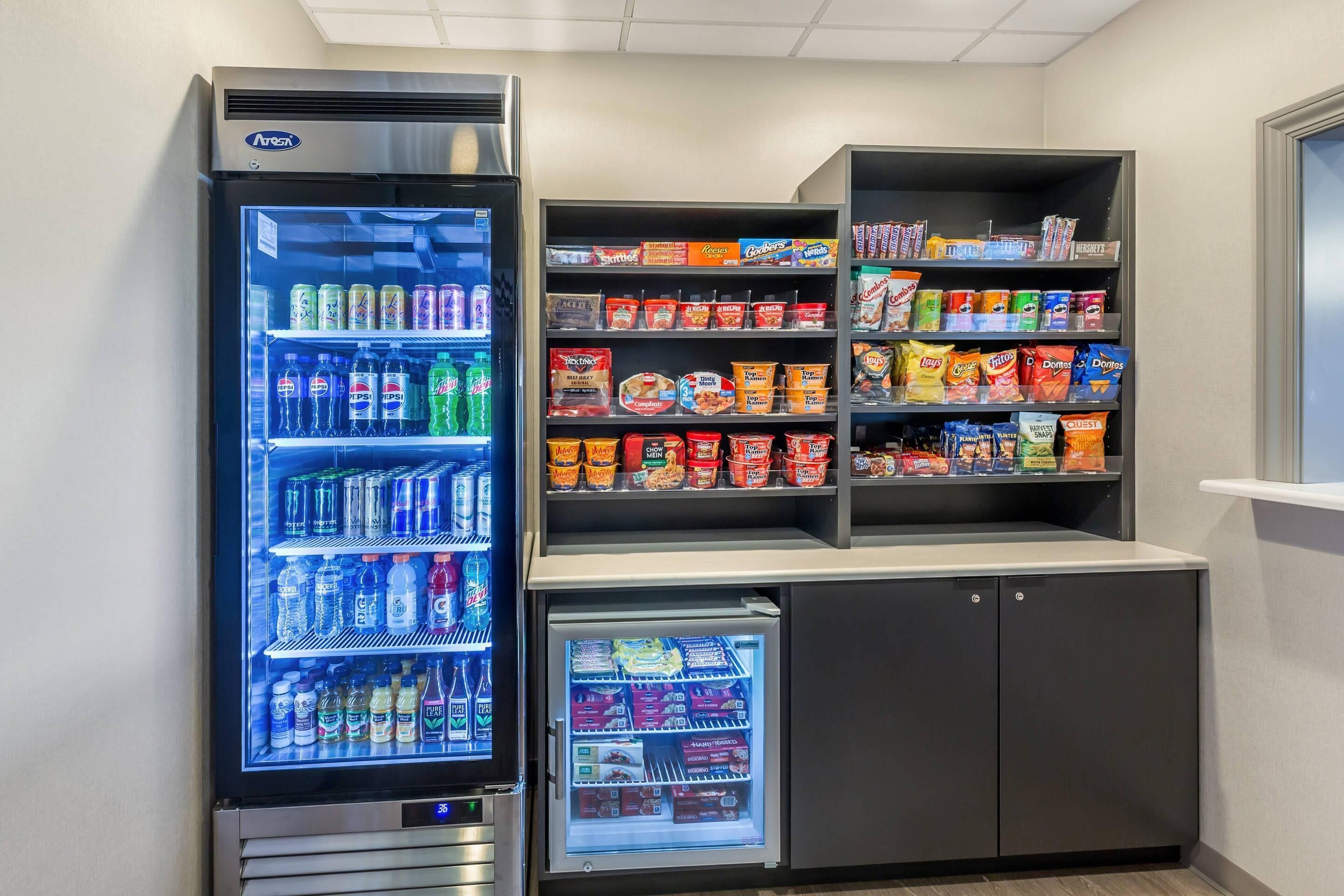 A vending machine with various beverages and snacks, a small refrigerator with snacks, and shelves stocked with packaged goods.