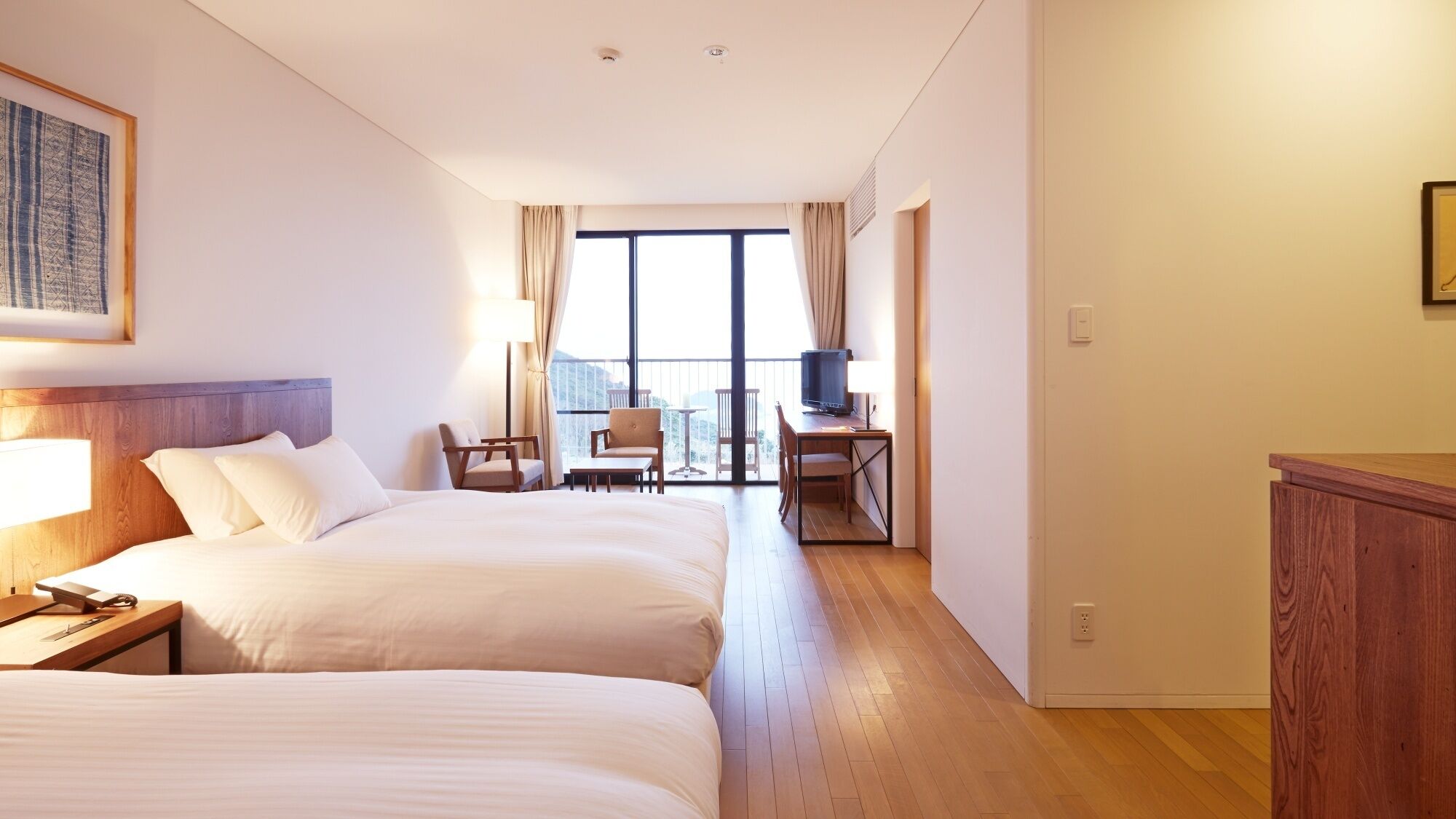 Une chambre d’hôtel avec deux lits, un bureau avec une télévision, une chaise et un balcon avec des rideaux.