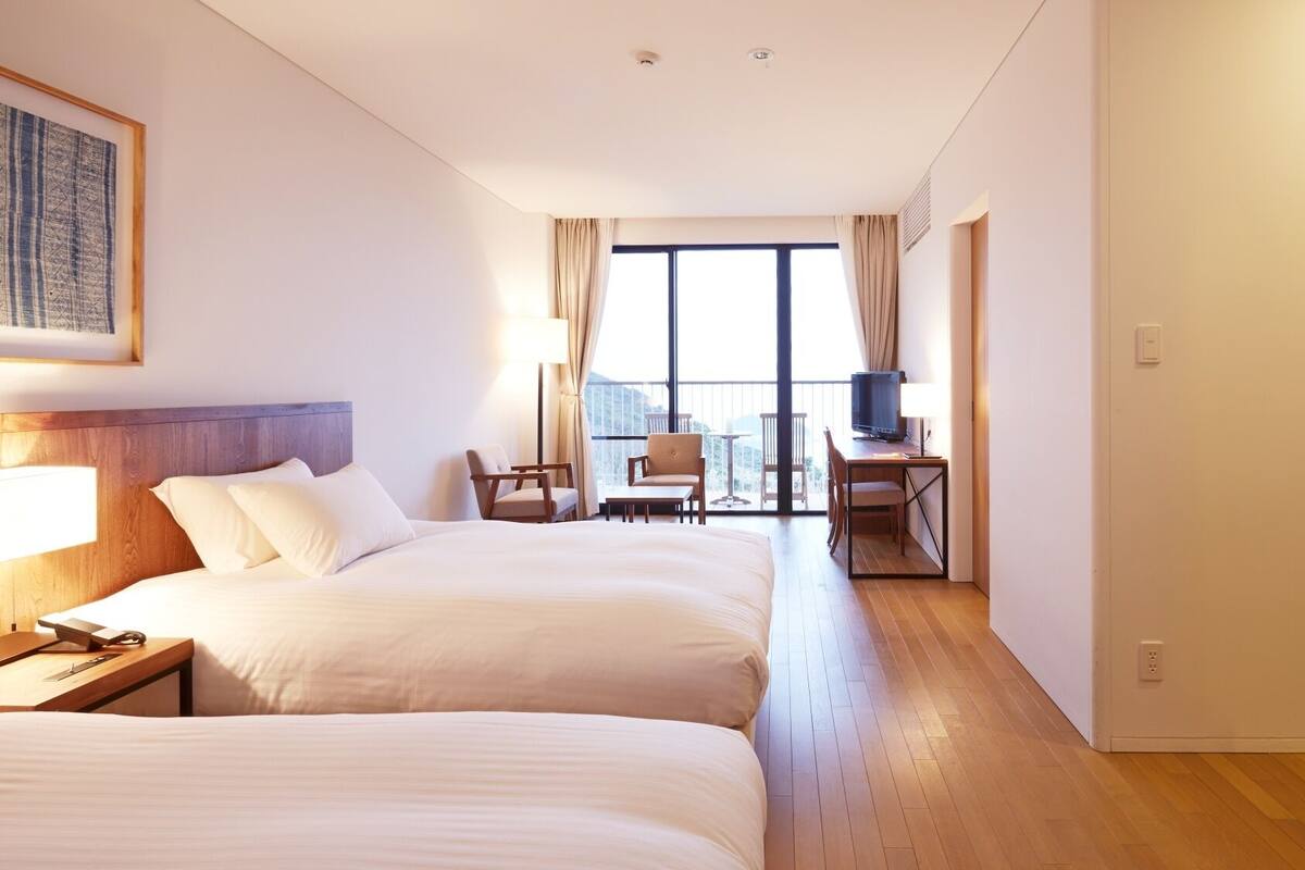 Ein Hotelzimmer mit zwei Betten, einem Schreibtisch, einem Fernseher und einem Balkon mit Blick.