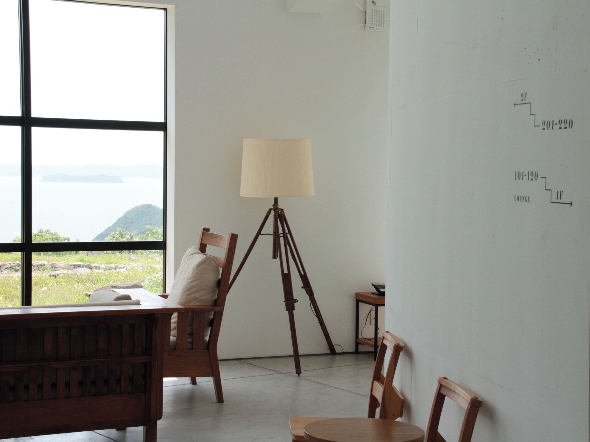 A room with a large window overlooking a body of water, a tripod lamp, and a whiteboard with floor plan markings.