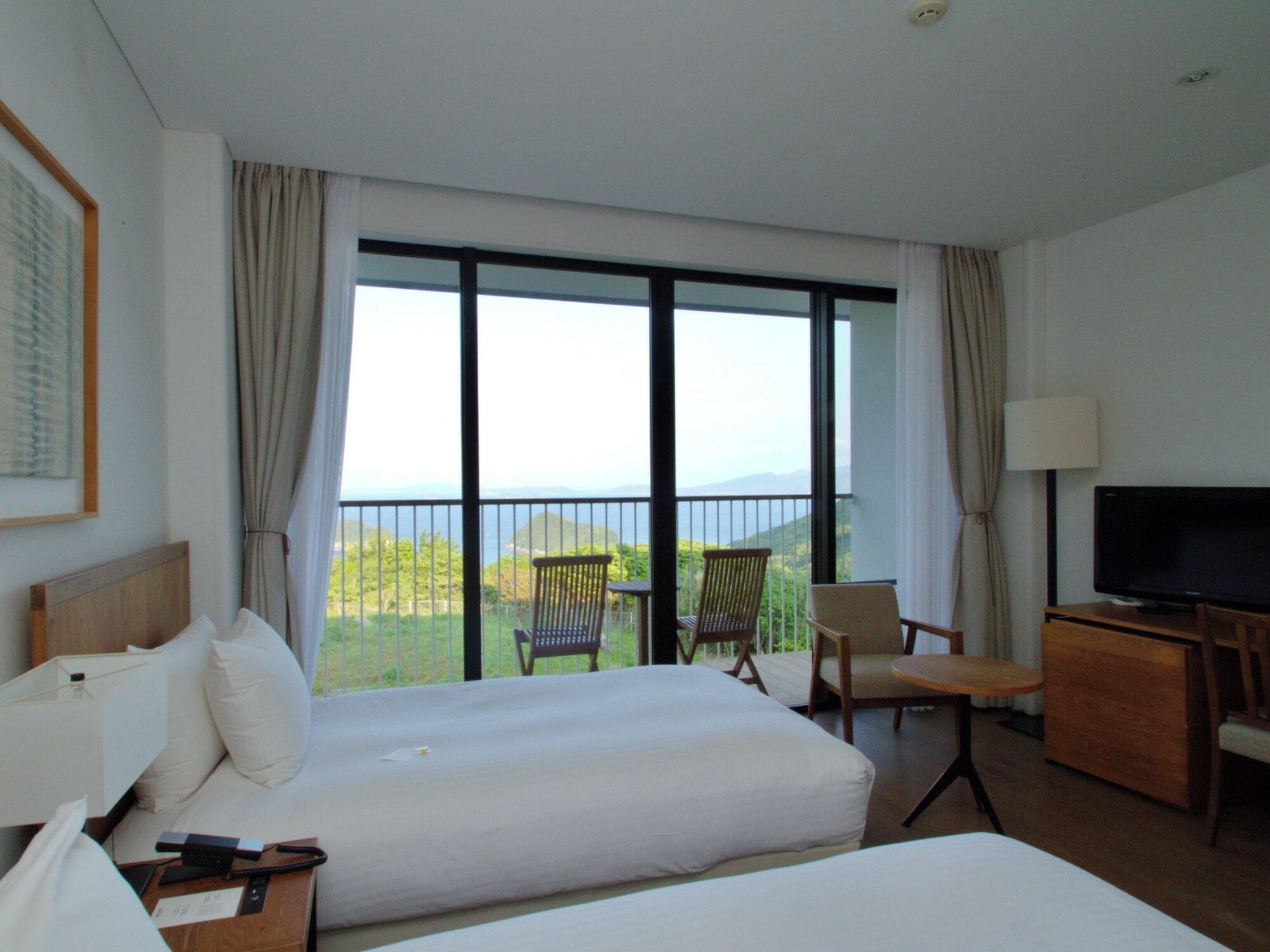 Une chambre d’hôtel avec deux lits, une télévision, un bureau et un balcon équipé de chaises.