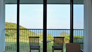 Ein Balkon mit zwei Holzstühlen und einem kleinen Tisch, mit Blick auf eine üppige, grüne Landschaft mit Hügeln und blauem Himmel.