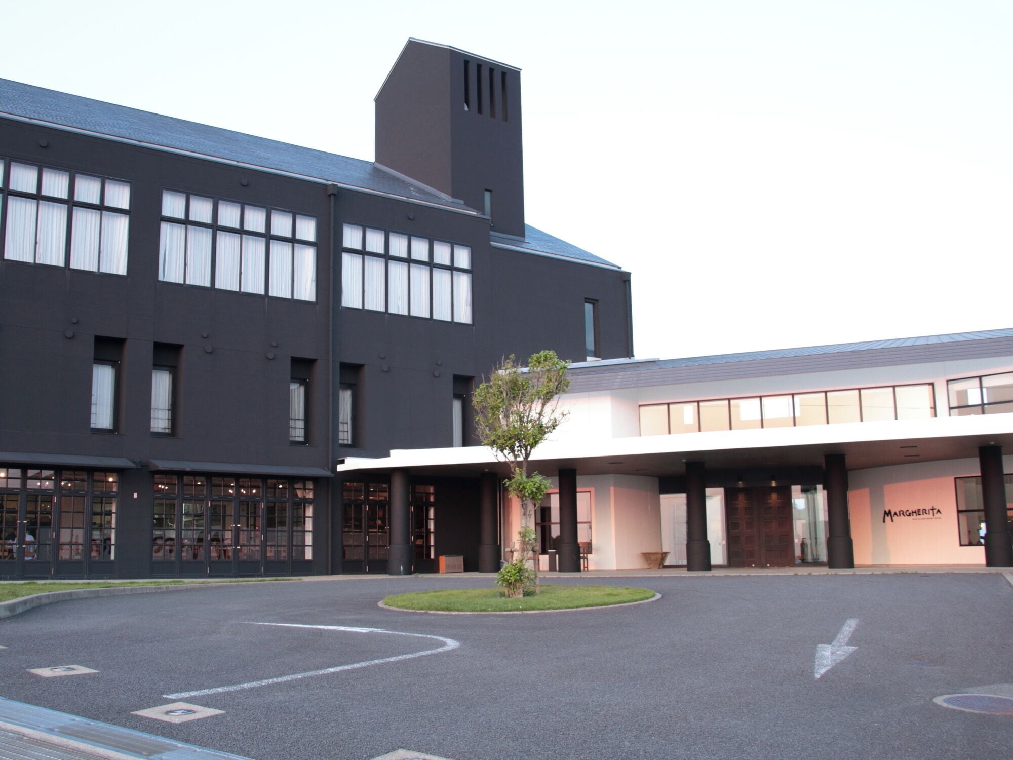A modern building with a black facade and large windows, a landscaped area with a tree, and a sign reading "MARGHERITA".