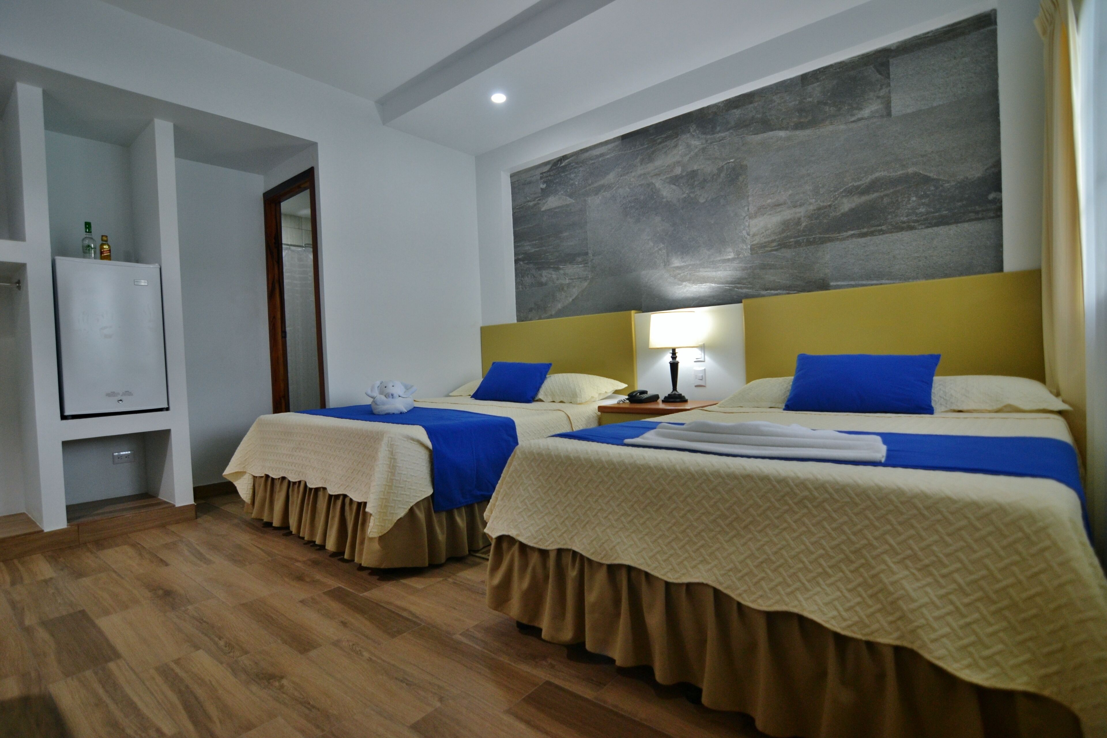 Habitación de hotel con dos camas, un armario, un espejo y una gran obra de arte abstracta en la pared.