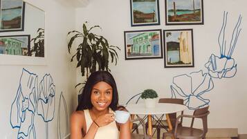 A woman sitting at a round table with a potted plant, surrounded by framed artwork and chairs.