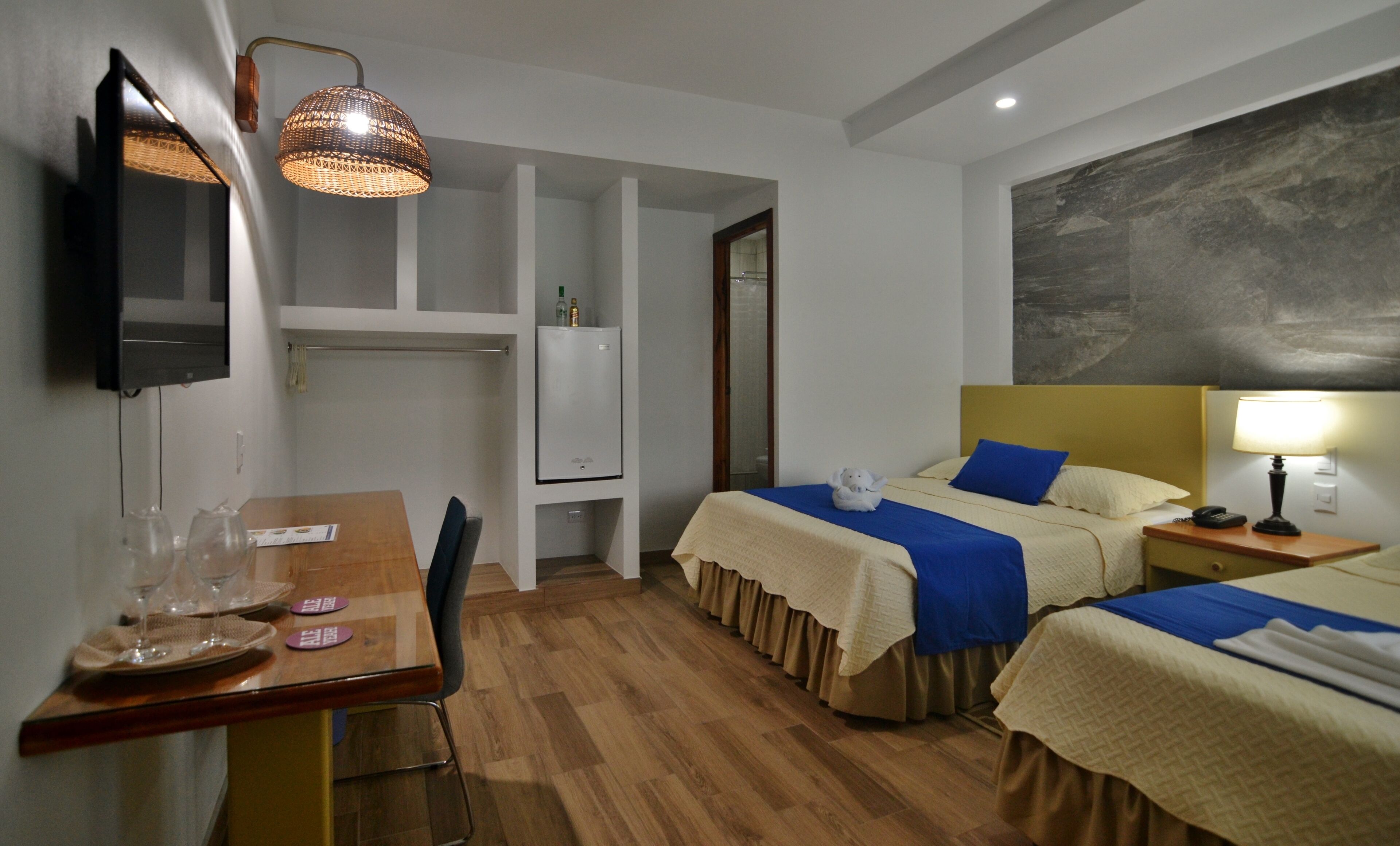 A hotel room with two beds, a desk with a chair, a television, a lamp, and a large painting on the wall.