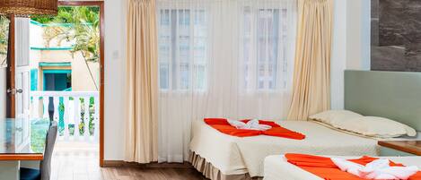 A hotel room with two beds, a wooden floor, a balcony with a view of palm trees, and a large window with curtains.