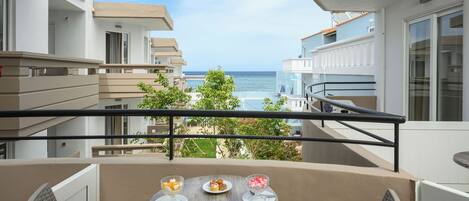 A balcony with a table set for two, overlooking a coastal view.