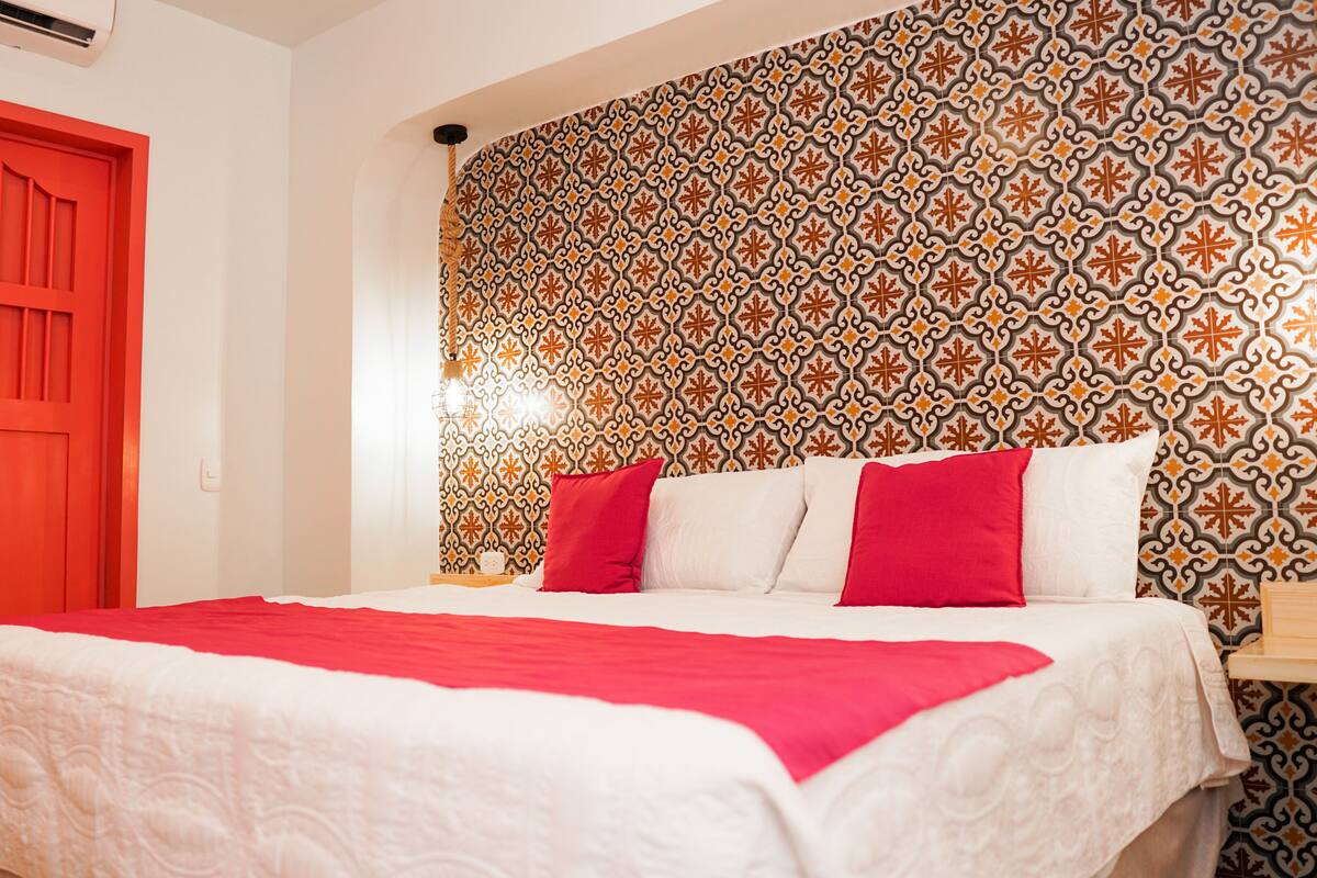 Una habitación de hotel con cama, una puerta roja y un papel tapiz estampado.