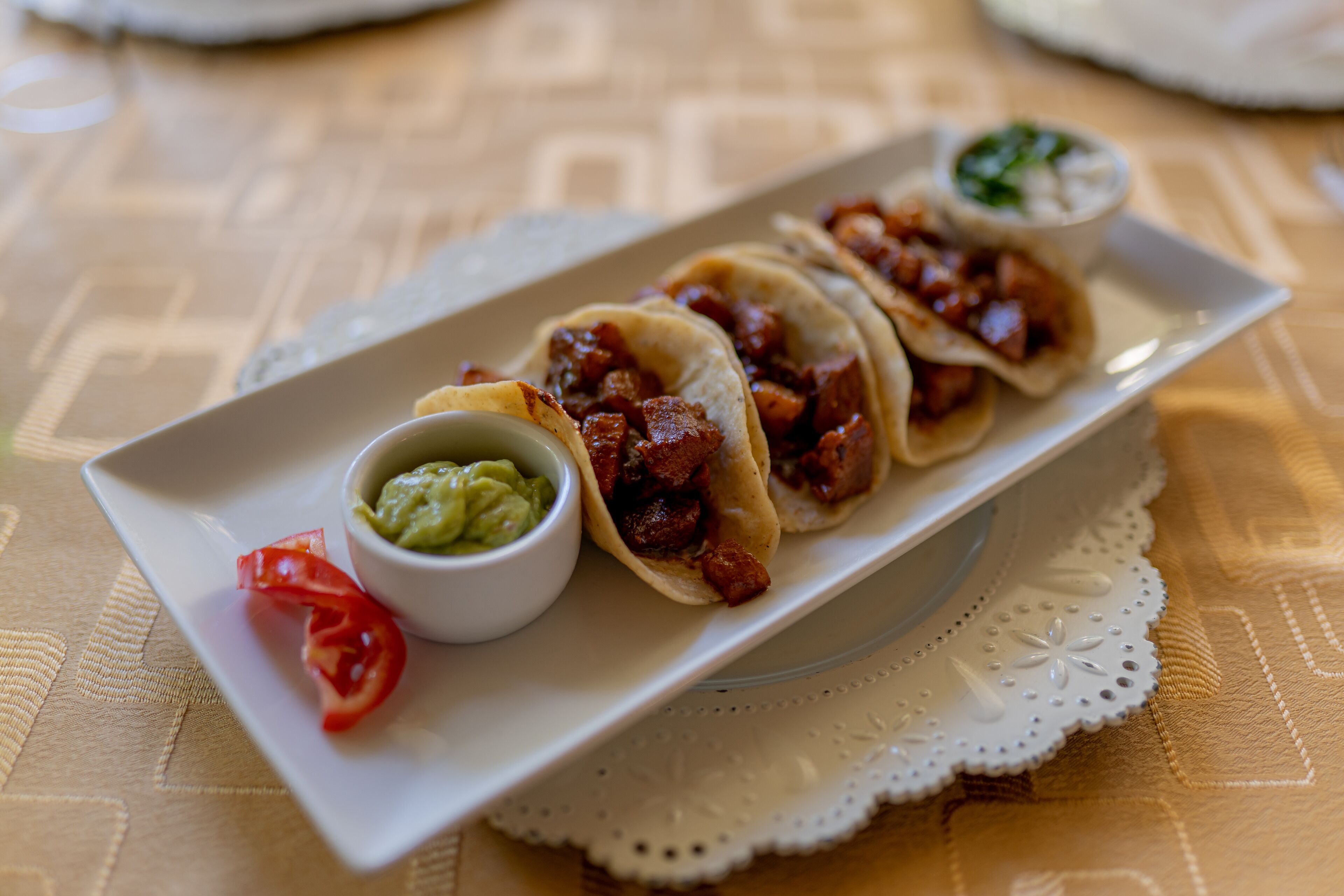 A plate with three tacos, a small bowl of guacamole, and a red chili pepper.