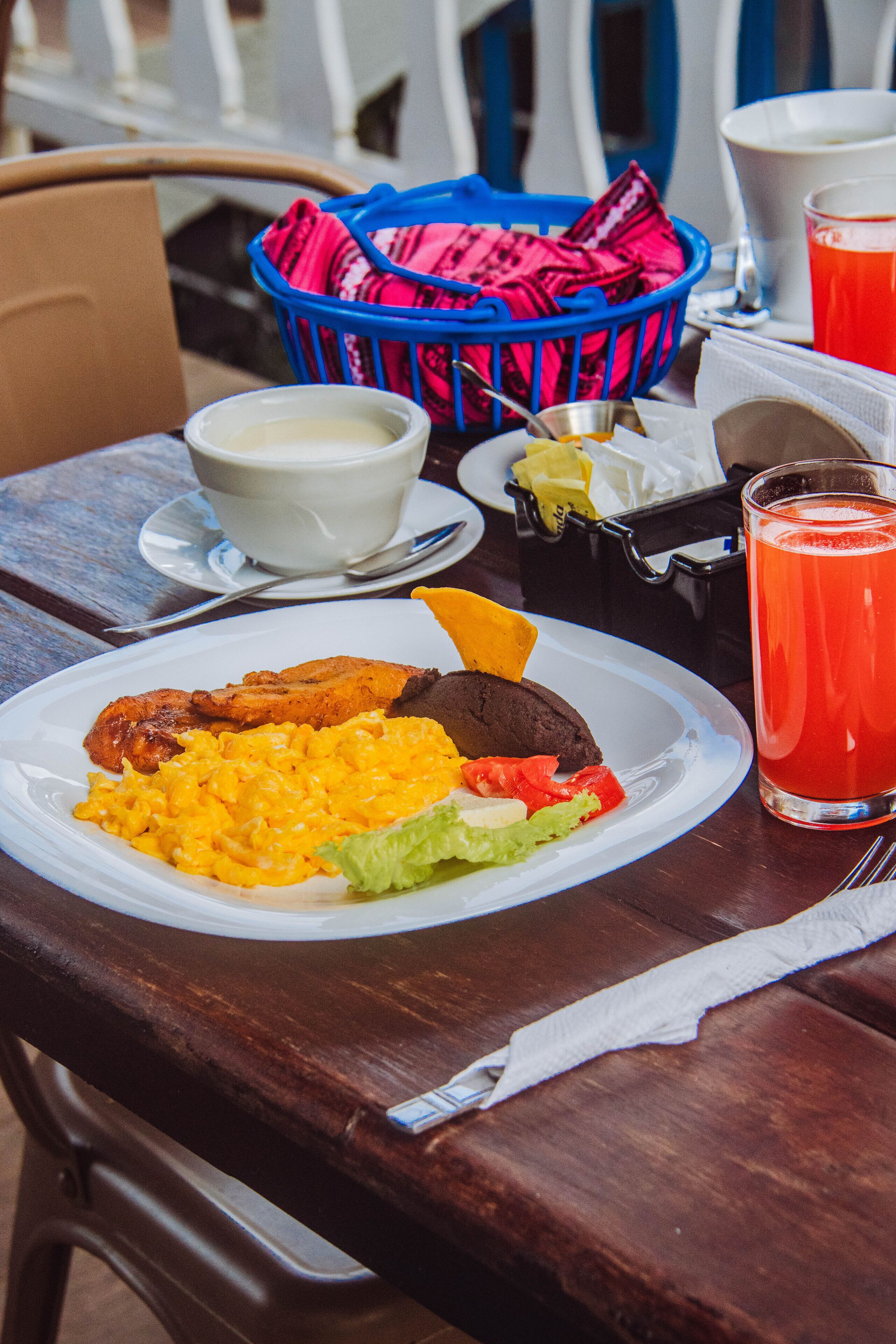 A table with a plate of food, a basket, a cup, and a glass of juice.