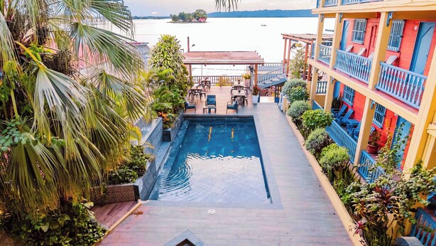 A pool area with lounge chairs and a hot tub, surrounded by palm trees and a building with balconies. - Hotel Casona de La Isla (Flores)