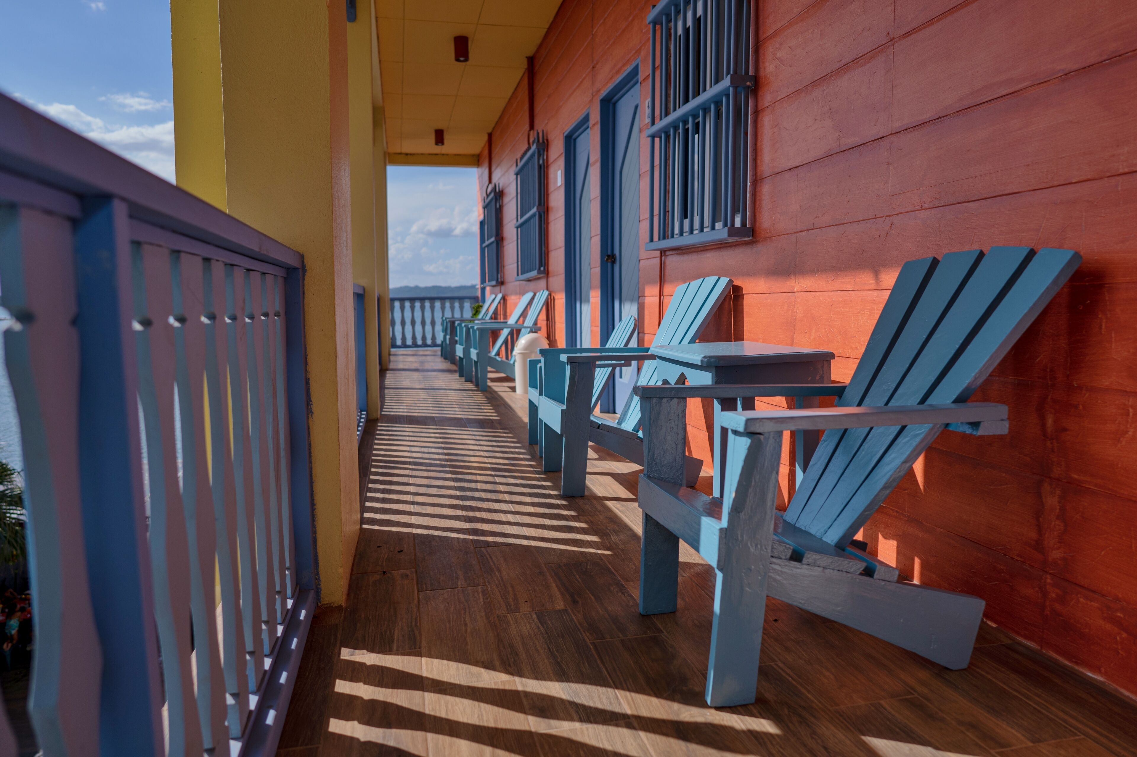 A balcony with wooden flooring and blue Adirondack chairs.