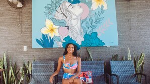 A person sitting on a wicker chair in front of a wall with a large floral and abstract painting. - Hotel Casona de La Isla (Flores)