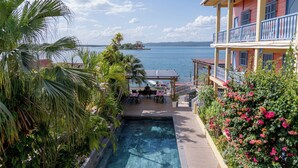 A pool area with a view of the sea, surrounded by tropical plants and a building with a balcony. - Hotel Casona de La Isla (Flores)