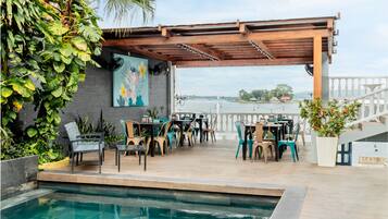 Eine Terrasss mit Pool, Holz-Pergola und Sitzbereich mit Stühlen und Tischen.